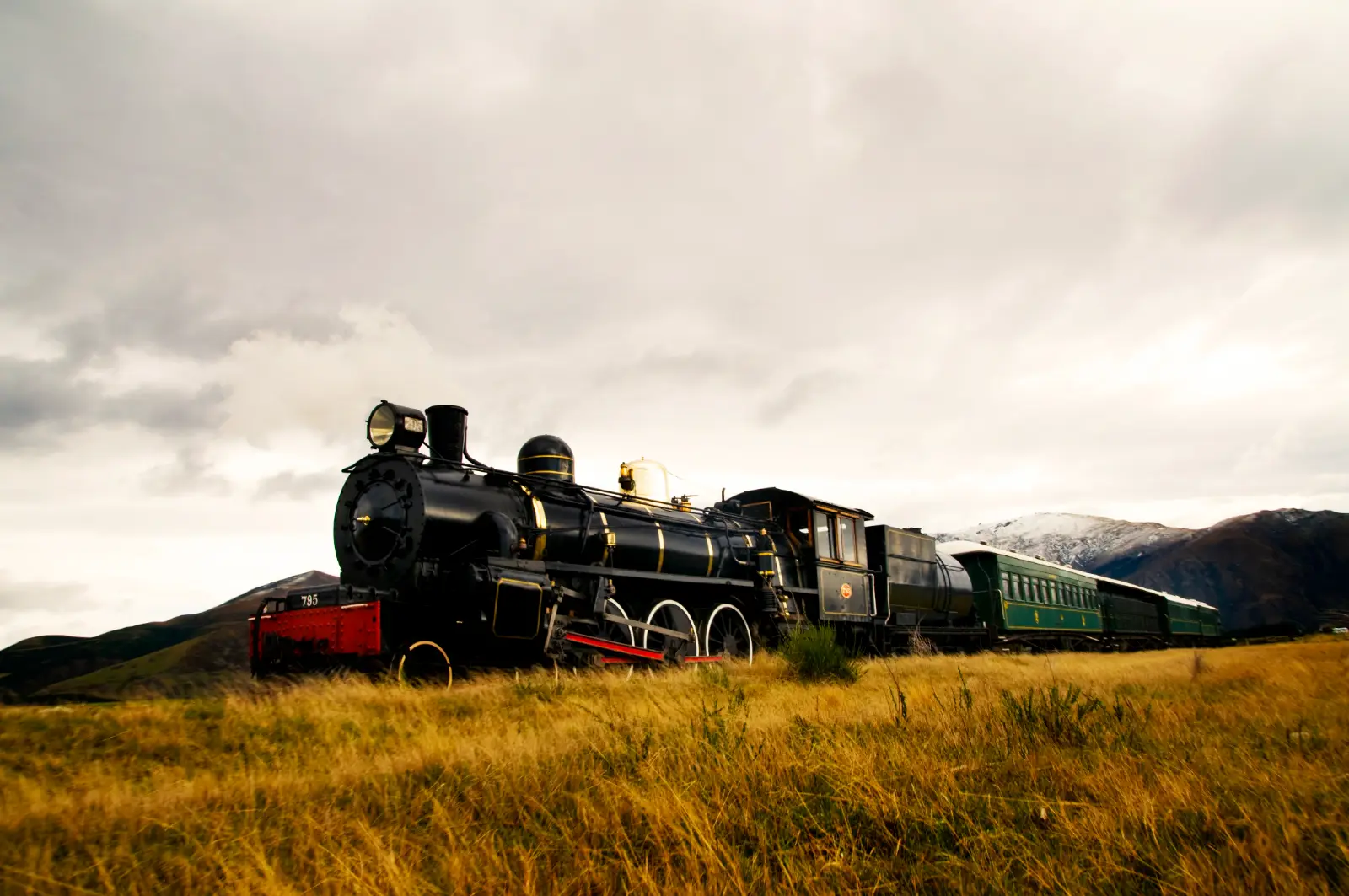 Steam locomotive pulling passenger cars through open countryside